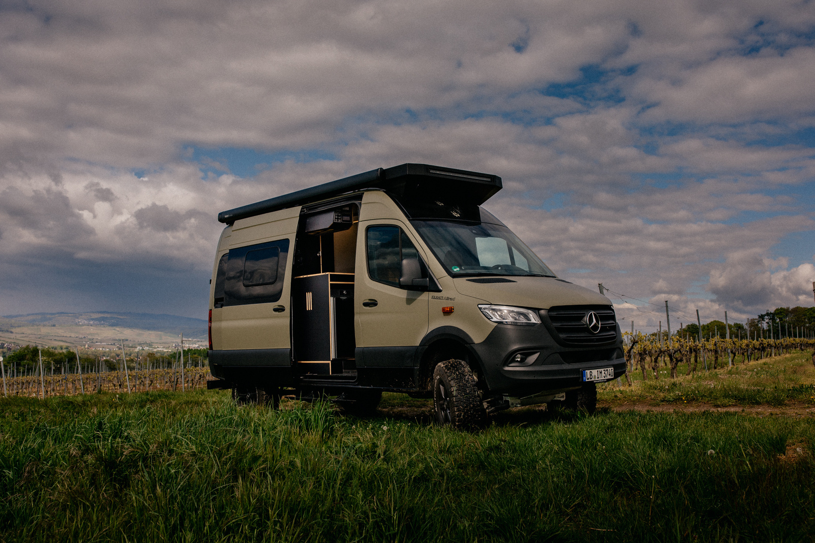 Design Campervan SAM the Van mit Iglhaut Allrad: Ein Campervan mit nachhaltigen Materialien, Schafwolle Dämmung und Sprühkork. Van steht in einem Weinberg, Tür geöffnet und Blick auf die Küchenzeile