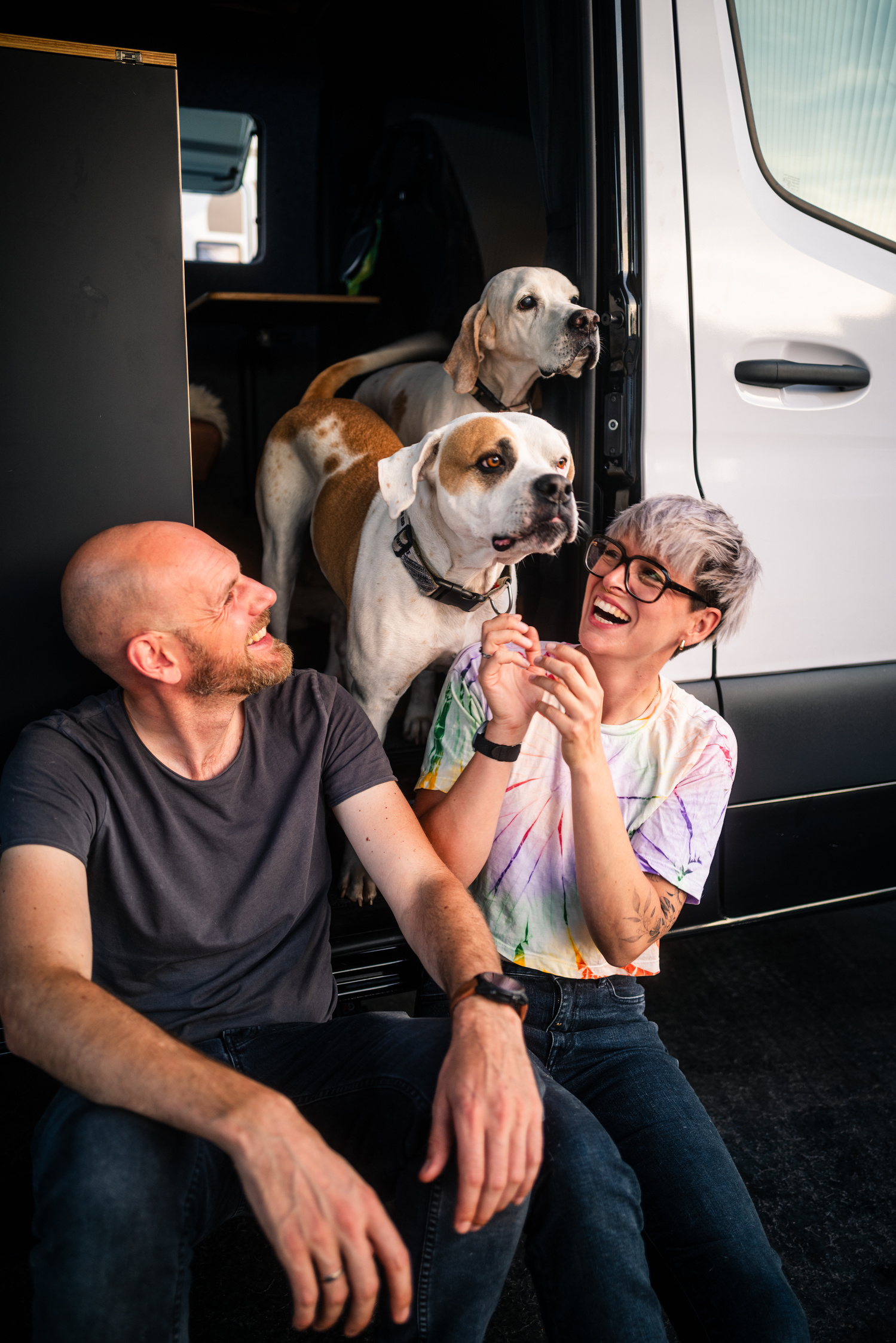 Architektin Maria Bauer und Designer Ingo Scheinhütte, Gründerin und Entwickler der SAM the Van GmbH und ihre zwei Hunde Lana und Bino sitzen lachend in einem SAM the Van Campervan, die SAM the Van Familie.